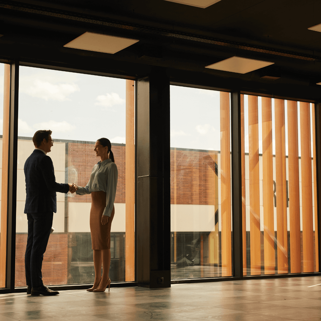 Man and woman in business attire shaking hands in a modern office, representing successful business partnerships and commercial agreements advised by Hebden Legal, serving Dunsborough, Vasse, and surrounding WA areas.